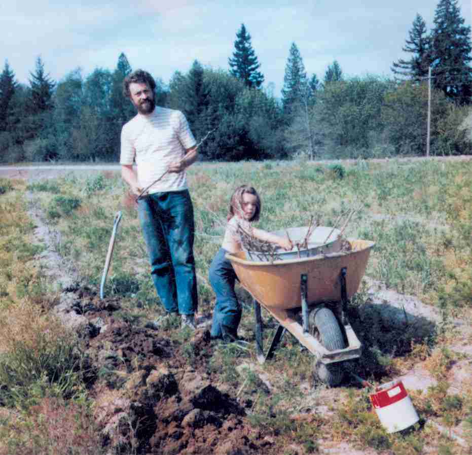 Man and child with a wheelbarrow in a field with trees in the background